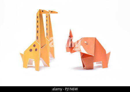 Three origami animals stand on a white background, two giraffes and one elephant Stock Photo