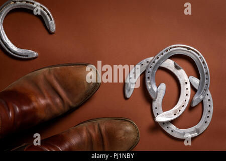 Horseshoes and a pair of leather shoes isolated on a brown background with copy space Stock Photo