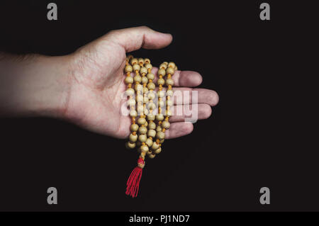 Wood sandalwood prayer beads in hand on black background. Stock Photo
