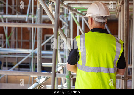 Rear view of male builder construction worker on building site wearing hard hat and hi vis vest Stock Photo