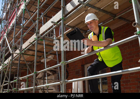 Male builder foreman, construction worker or architect on site holding a clipboard and drinking a mug of coffee or tea Stock Photo