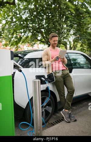 Man using digital tablet while charging electric car Stock Photo
