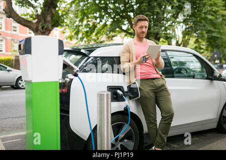 Man using digital tablet while charging electric car Stock Photo