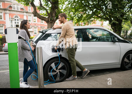 Couple interacting with each other while charging electric car Stock Photo