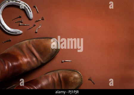 Horseshoe, nails, and a pair of leather shoes isolated on a brown background with copy space Stock Photo