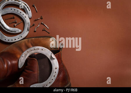 Horseshoes, nails, and a pair of leather shoes isolated on a brown background with copy space Stock Photo