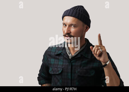 Confident man in knitted hat pointing finger upwards over white background. Stock Photo