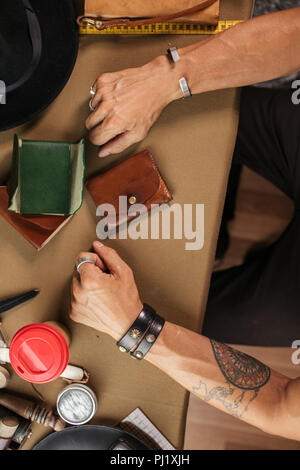 Leather goods master and handmade leather wallets. Workflow in the workshop. Stock Photo