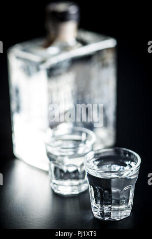 Vodka in shot glass. Transparent alcohol on black table. Stock Photo