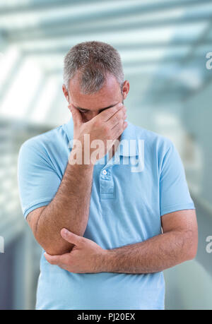 Depressed Concept. Displeased young man in blue shirt covering his eyes Concept of negative emotion. Problems at work or in family Stock Photo