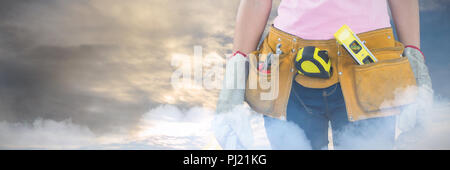 Composite image of woman with tool belt and holding hard hat against grey background Stock Photo