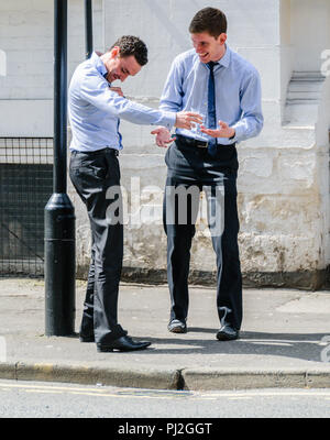 Two young, smart men laughing with each other in a street in Manchester during a break from the office Stock Photo