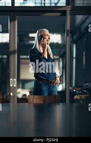 Smiling mature businesswoman in casuals talking on cell phone. Senior female executive in office making a phone call. Stock Photo