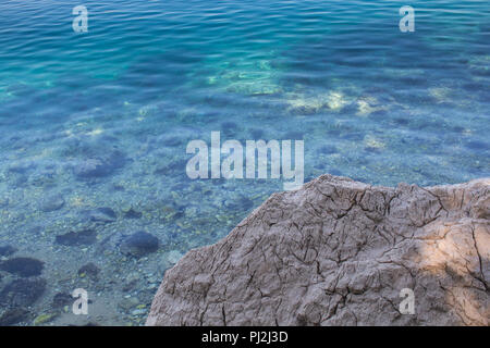 Rock with cracks on the coast of Adriatic sea. Turquoise color of the sea water in the distance. Thanks to the clean and clear water visible stones on Stock Photo