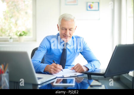 Smiling senior businessman doing some paperwork while sitting at office desk and working on presentation. Stock Photo