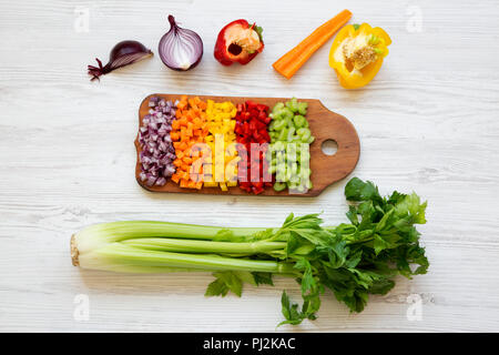 Chopped fresh vegetables (carrot, celery, onion, colored peppers) arranged on cutting board on white wooden background, top view. From above, overhead Stock Photo