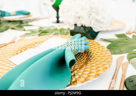 Interior of tent for wedding diner, ready for guests. Served round banquet table outdoor in marquee decorated hydrangea flowers, Golden dishes and green napkins. Catering concept Stock Photo