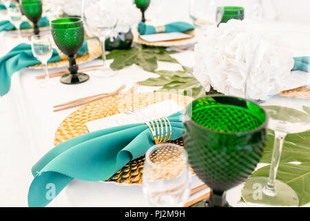 Interior of tent for wedding diner, ready for guests. Served round banquet table outdoor in marquee decorated hydrangea flowers, Golden dishes and green napkins. Catering concept Stock Photo