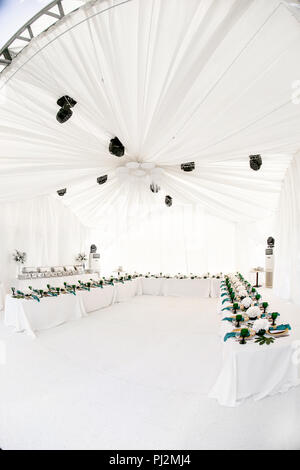 Interior of tent for wedding diner, ready for guests. Served round banquet table outdoor in marquee decorated hydrangea flowers, Golden dishes and green napkins. Catering concept Stock Photo