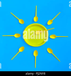 A yellow plastic plate and spoons lay around it on a bright blue background. The concept of a holiday, picnic Stock Photo