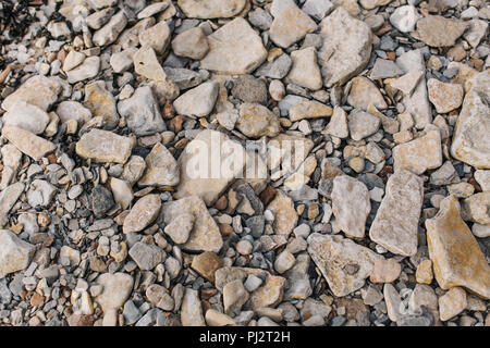 Looking down at the surface of a rocky beach with many rocks, stones and pebbles of different shapes and sizes in muted brown and orange colours Stock Photo