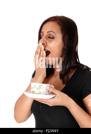 A beautiful young woman holding a coffee cup in her hand and yawning with her hand over her mouth, isolated for white background Stock Photo