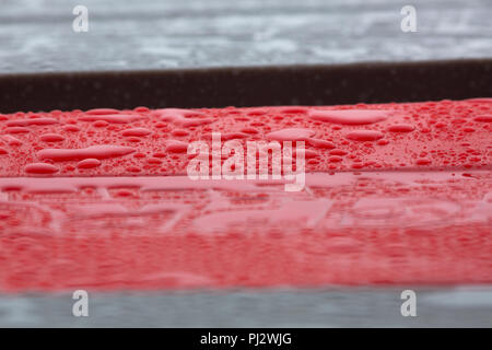 Raindrops pooled together on top of a red barrier Stock Photo