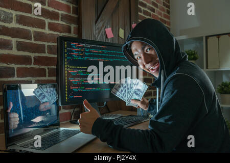 haker giving a thumb up and holding paper money in hands in his basement with enjoyment. Stock Photo