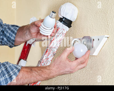 Electrician technician working on the ladder to replace the fluorescent lamp of a ceiling light with a new LED bulb in a residential electrical system Stock Photo