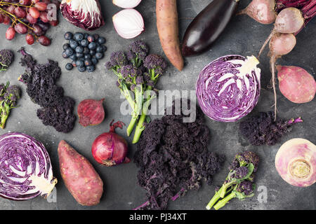 Vegetables and fruits background in purple, green and dark red colours, cabbage kale sprouts sweet potato onions broccoli blueberries grapes, top view, dark grey background, selective focus Stock Photo