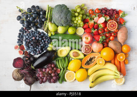 Healthy eating concept, assortment of rainbow fruits and vegetables, berries, bananas, oranges, grapes, broccoli, beetroot on the off white table arranged in a rectangle, top view, selective focus Stock Photo