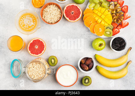 Healthy breakfast with oats, fruits, strawberries, mango, grapes, figs, yogurt and nuts arranged in a circle frame served on the grey white table, top Stock Photo