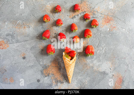 Ice cream cone filled with strawberries, overhead composition with berries on the grey stone background Stock Photo