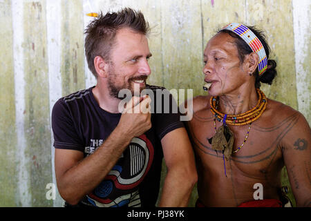 Male tourist making friends showing his beard to a Mentawai man smoking , Siberut, Sumatra, Indonesia Stock Photo