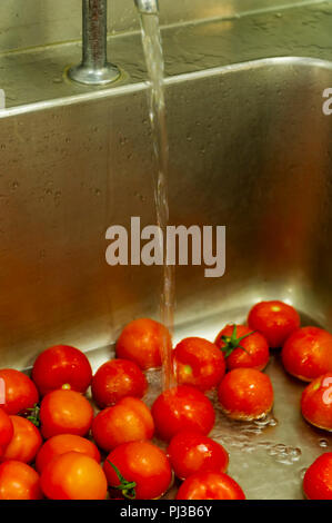 Tomatoes being washed under running water in a sink Stock Photo