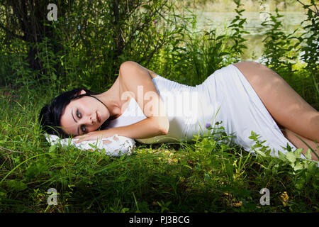 Pale woman in white dress lying on the ground, fairytale scene Stock Photo