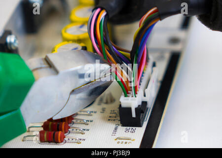 Dismantling electronic bomb, tongs cut the red wire into a bundle of colored wires on the background of the motherboard or electronic chip Stock Photo