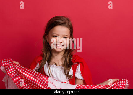 A small girl in Little Red Riding Hood costume in studio on a red background. Stock Photo