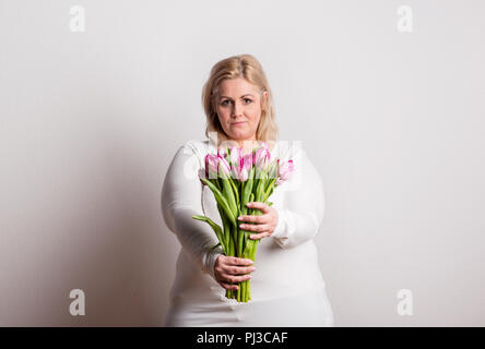 Portrait of an attractive overweight woman with tulips in studio on a white background. Stock Photo