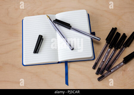 Blank lined notebook with some black biro pens on a light wood background Stock Photo