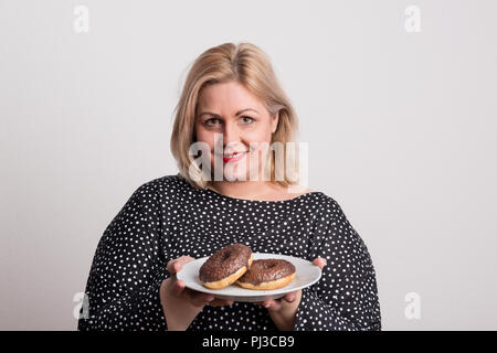 An attractive overweight woman in studio, holding donuts on a plate. Stock Photo