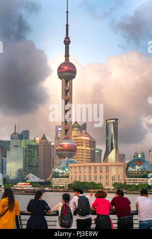 A group of Chinese tourists lean on railing of The Bund in Shanghai, China and look across the river to the Pudong skyline to watch sunset. Stock Photo