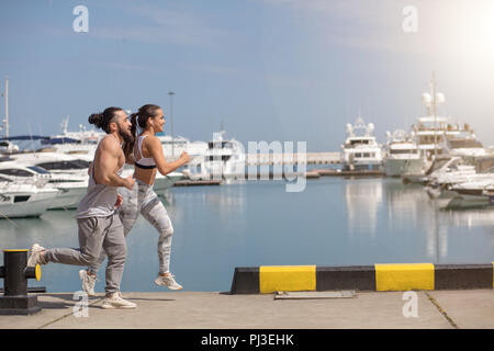 Young sporty couple running over wooden pier at sunset Stock Photo