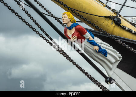 Glasgow, Scotland, UK - June 17, 2012: Closeup of figurehead representing blonde woman with gray dress, maroon vest and blue scarf, on the bow of Tall Stock Photo