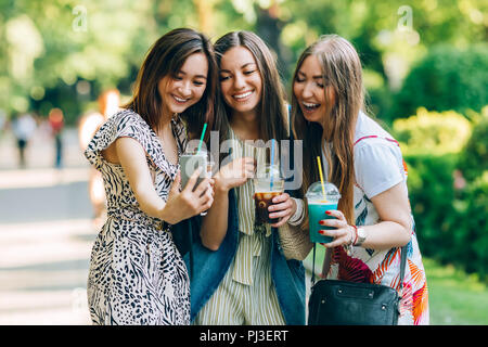 Summer lifestyle portrait multiracial women enjoy nice day, holding glasses of milkshakes. Happy friends in the park on a sunny day. Best friends girls having fun, joy. Lifestyle. Asian, jewess and caucasian. Stock Photo