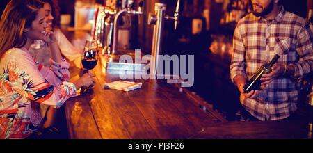 Bartender showing wine bottle to women at counter Stock Photo