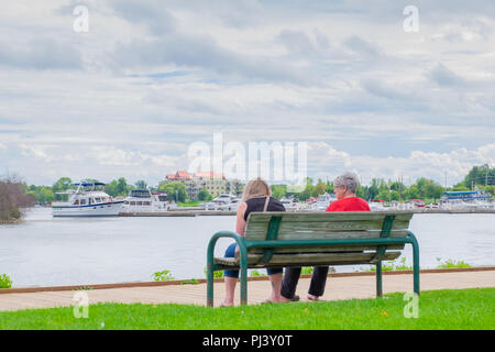 Two women sit on a bench near the boardwalk along the shore of Lake Couchiching at Orillia Ontario Canada. Stock Photo
