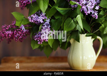Home interior decor, bouquet of lilacs in a vase and books on rustic wooden table, on a white wall background Stock Photo