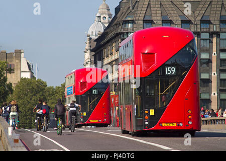 Rear view of a pair of New Routemaster red double decker London buses passing some cyclists on Westminster Bridge. Stock Photo