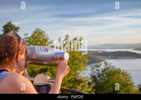 Young woman looking through tourist binocular telescope observing Oslofjord from the Ekeberg hill at sunset, Oslo, Norway Stock Photo